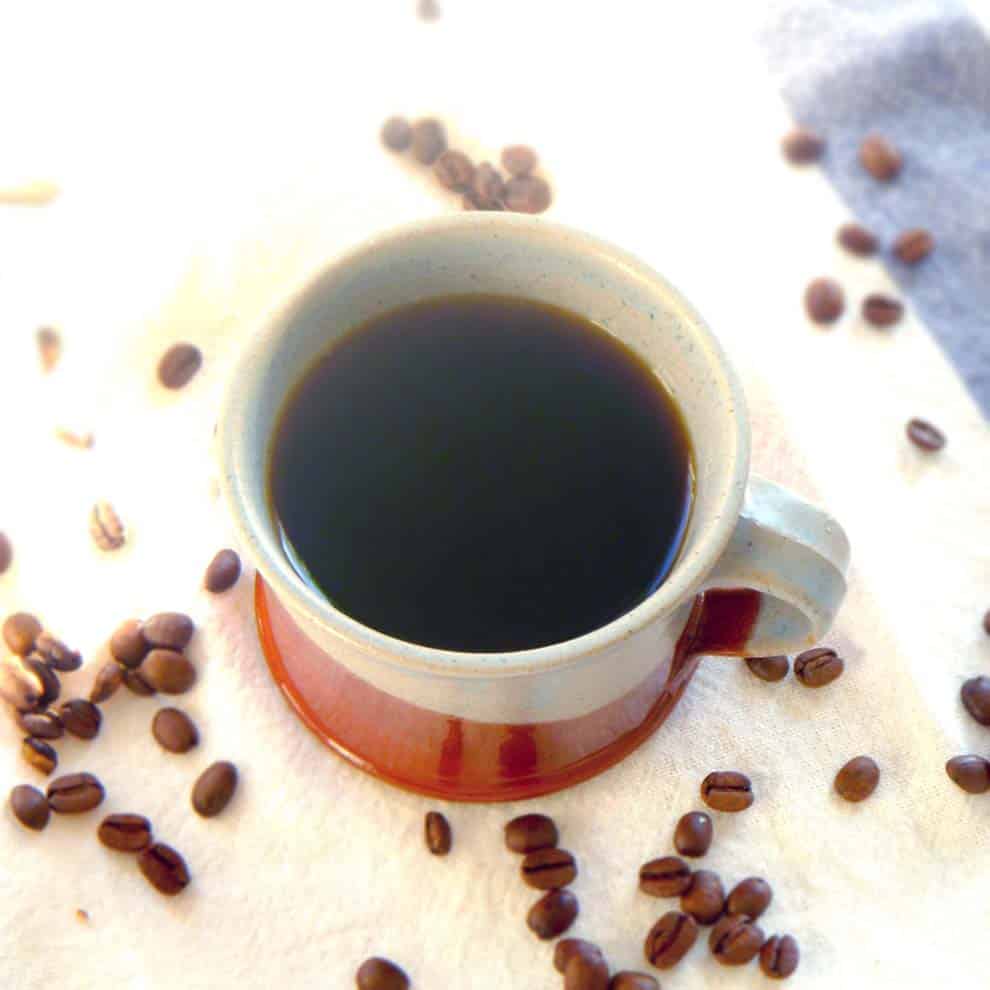 A mug of black coffee with coffee beans around it.