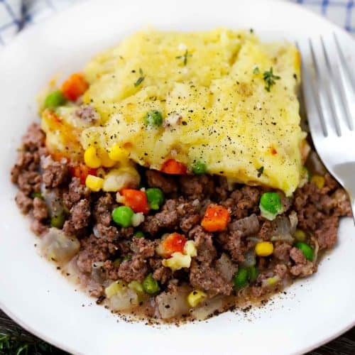 A close up photo of a white plate with shepherd's pie and a fork.