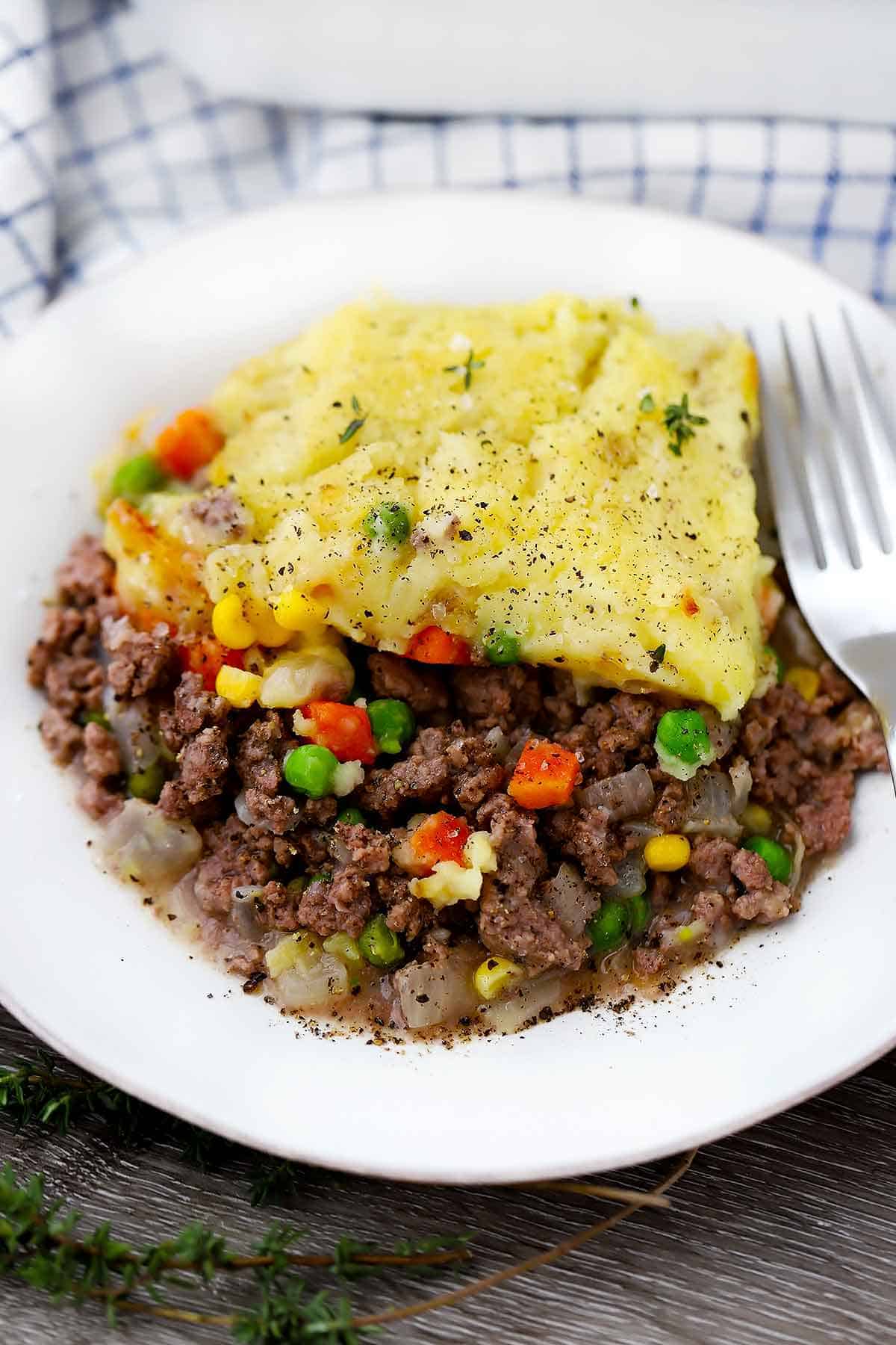 A close up photo of a white plate with shepherd's pie and a fork.