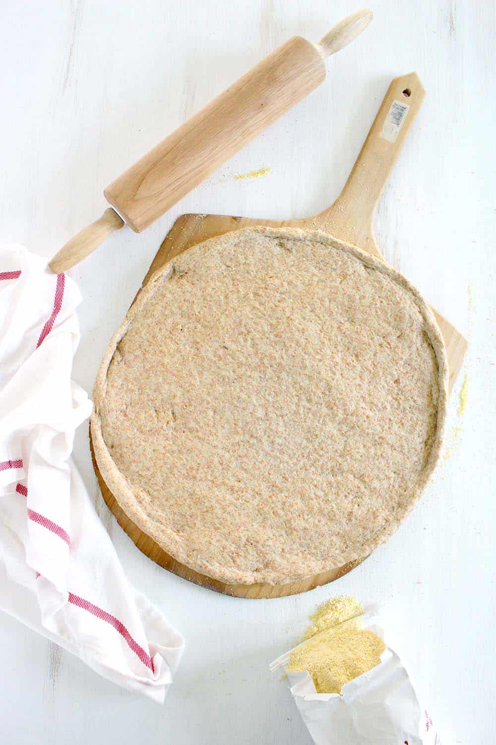 Flattened, rolled-out whole wheat pizza dough on a wooden pizza peel.