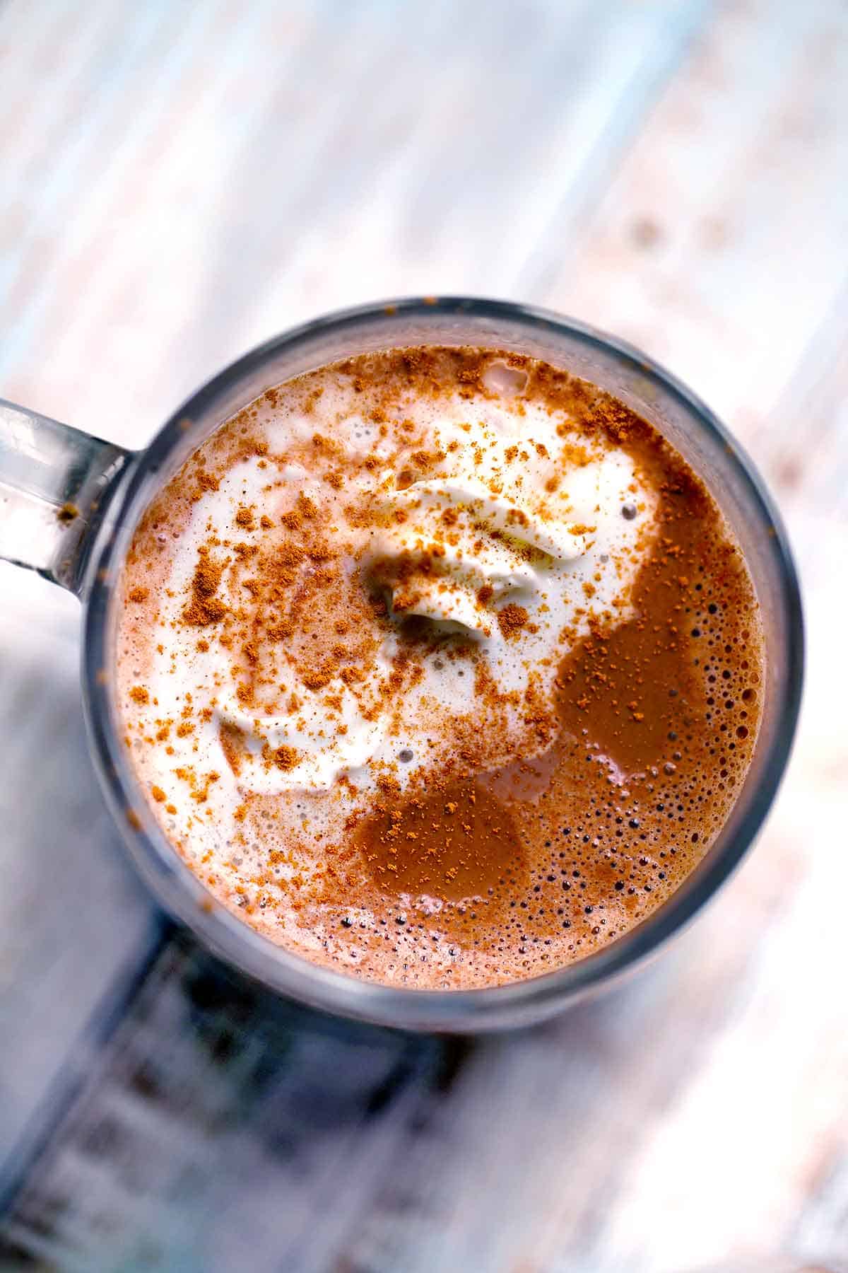 Overhead photo of a mug of spicy hot chocolate with whipped cream and cinnamon on top.