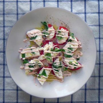 Plate of tomato slices topped with mozzarella slices, basil, and creamy sauce.