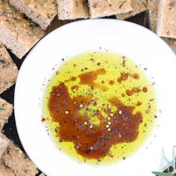 Close up photo of live oil, balsamic vinegar, and herbs in a shallow white bowl surrounded by pita chips.