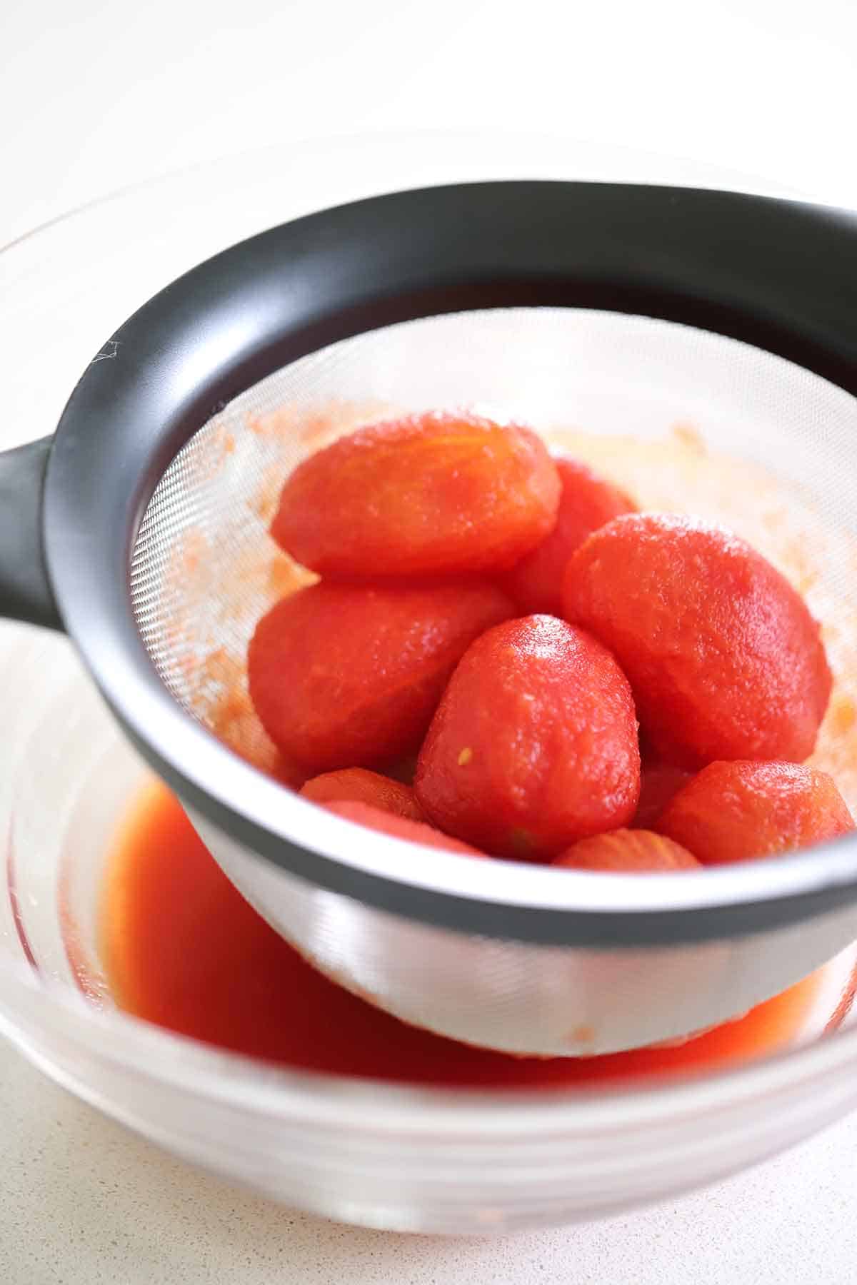 Draining whole canned tomatoes in a colander over a bowl.