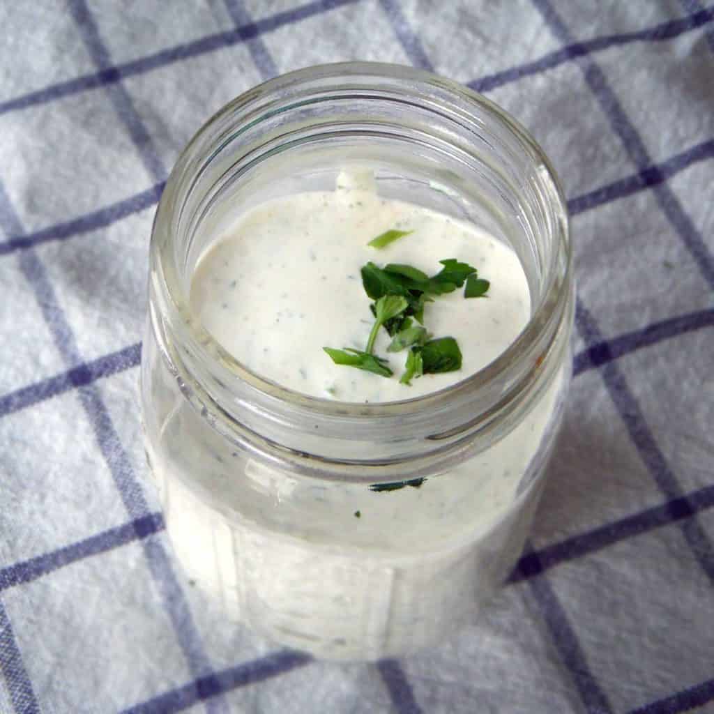 Glass jar of ranch dressing topped with herb garnish.