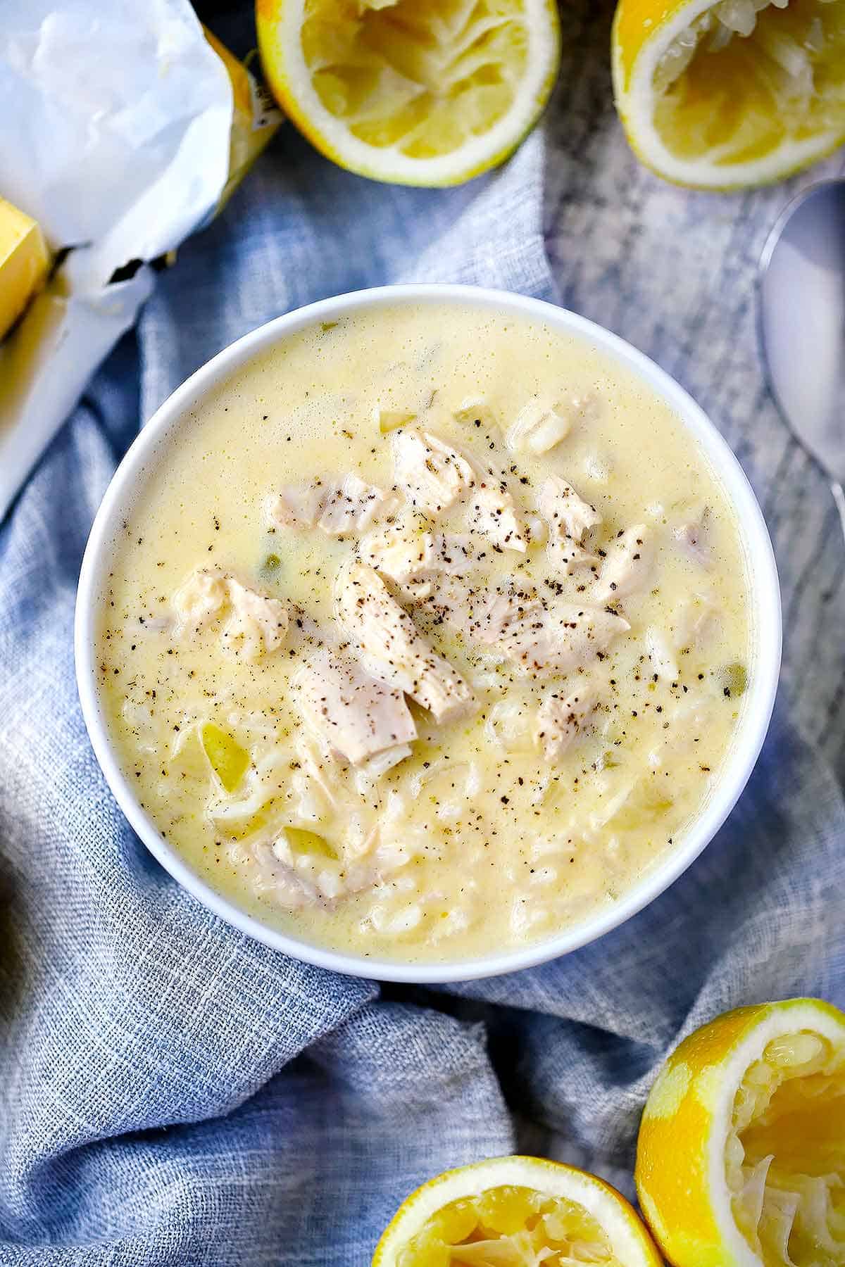 Overhead photo of a white bowl of Avgolemono soup with lemons around it.