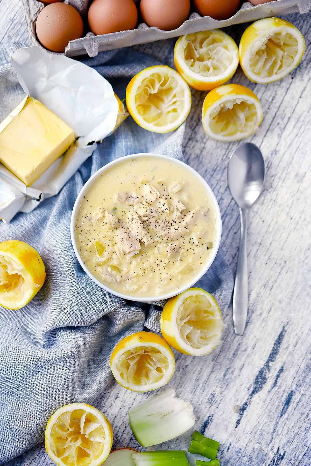 Overhead flatlay photo of a bowl of Greek chicken lemon egg soup with lemons, butter, and eggs around it.