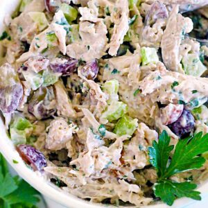 Square photo of a close up bowl of chicken salad with grapes and a parsley sprig.