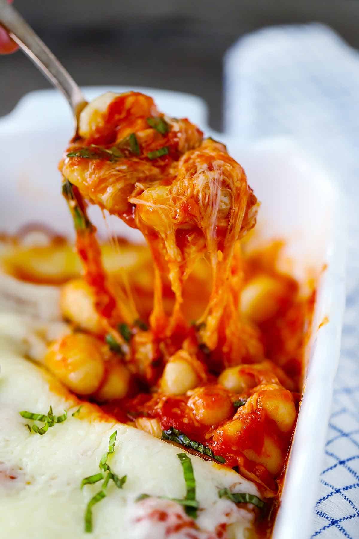 Scooping baked gnocchi out of a baking dish with cheese pull.