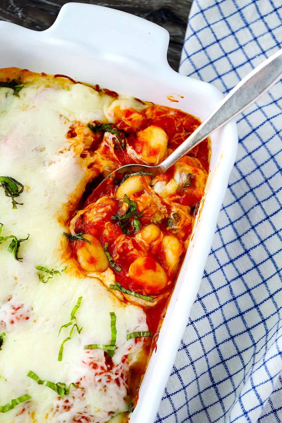 Gnocchi baked with marinara sauce, fresh basil, and cheese, with a spoon in a baking dish.