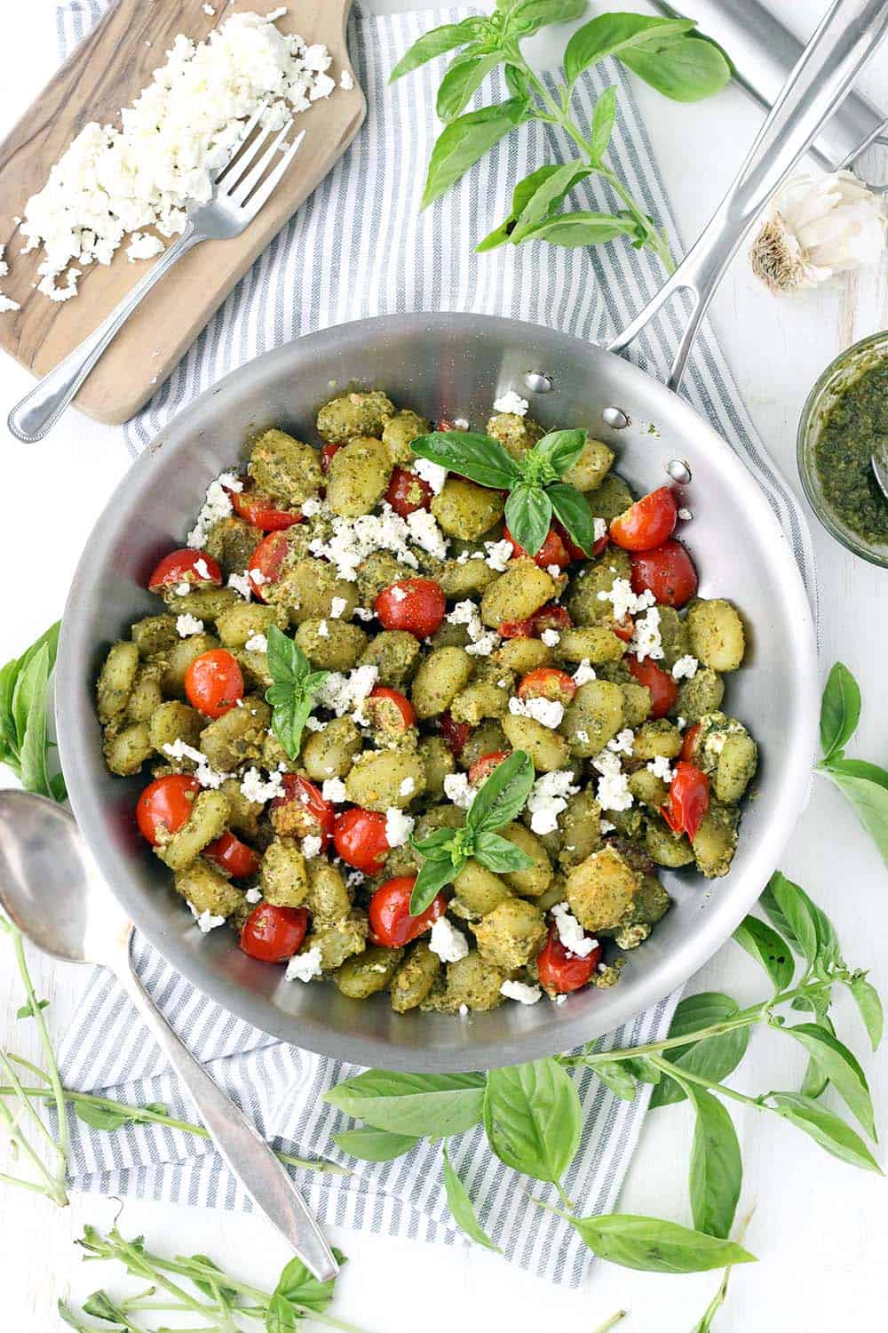 Pesto coated gnocchi with cherry tomatoes and goat cheese in a steel pan,  viewed from above.