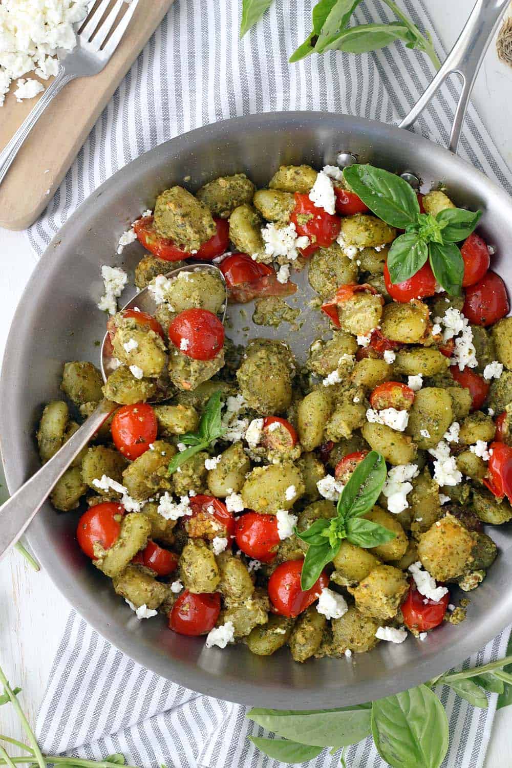 Closeup of pesto coated gnocchi in a steel pan with cherry tomatoes and goat cheese.