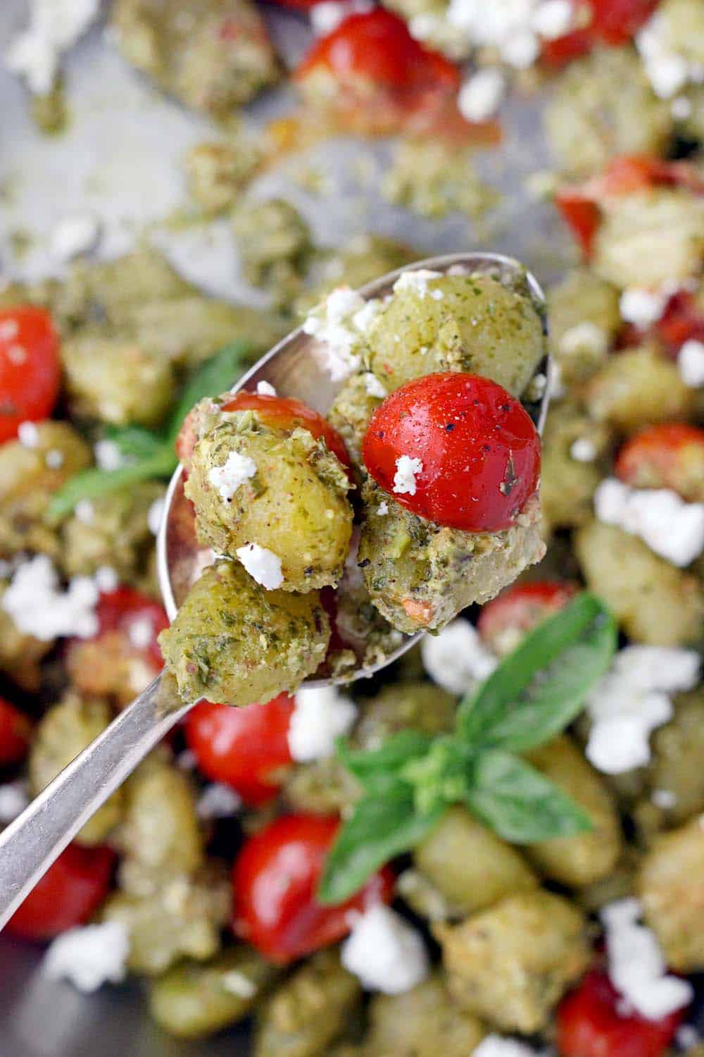 Close up of spoon full of pesto-coated gnocchi, cherry tomatoes, and goat cheese.