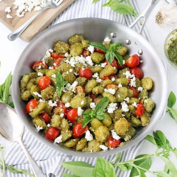 Pesto coated gnocchi with cherry tomatoes and goat cheese in a steel pan, viewed from above.