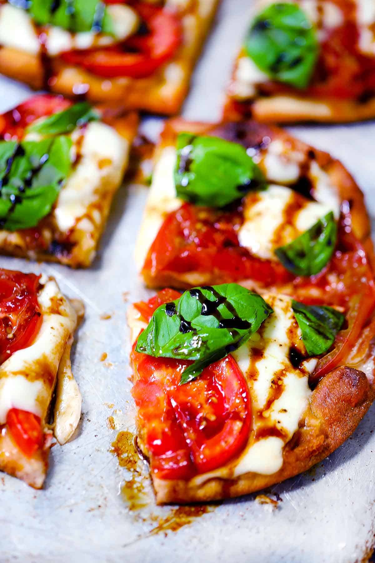 Close up photo of a sliced naan pizza with mozzarella, tomatoes, basil, and balsamic glaze on it.