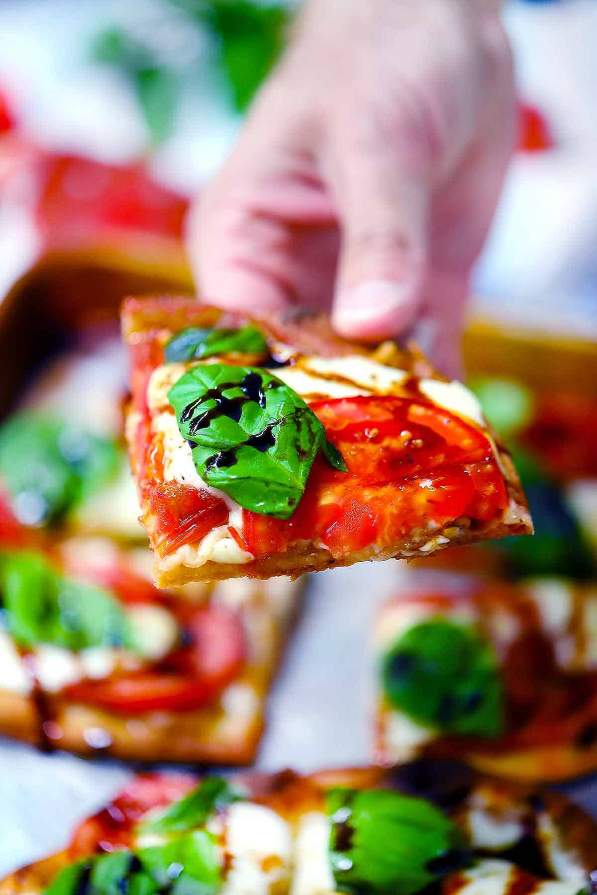 A hand holding a slice of caprese naan pizza.