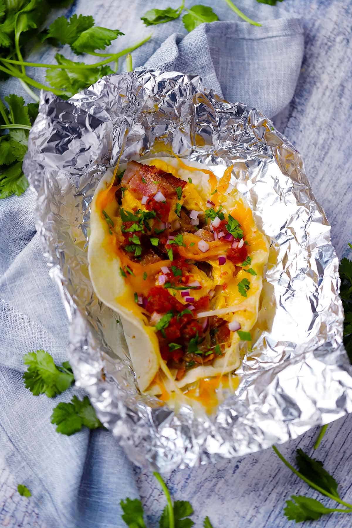 Breakfast taco with eggs, bacon, and cheese unwrapped from foil.