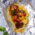 Square photo of a breakfast taco open on a piece of unwrapped foil.