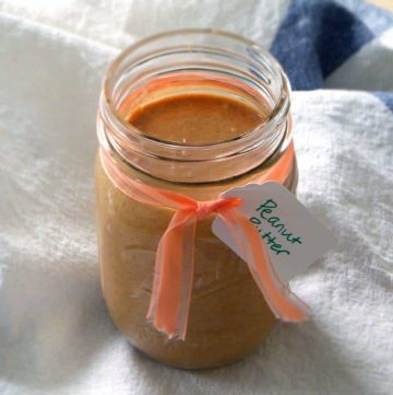 Open glass jar filled with peanut butter on white cloth, with orange ribbon tied around the jar.