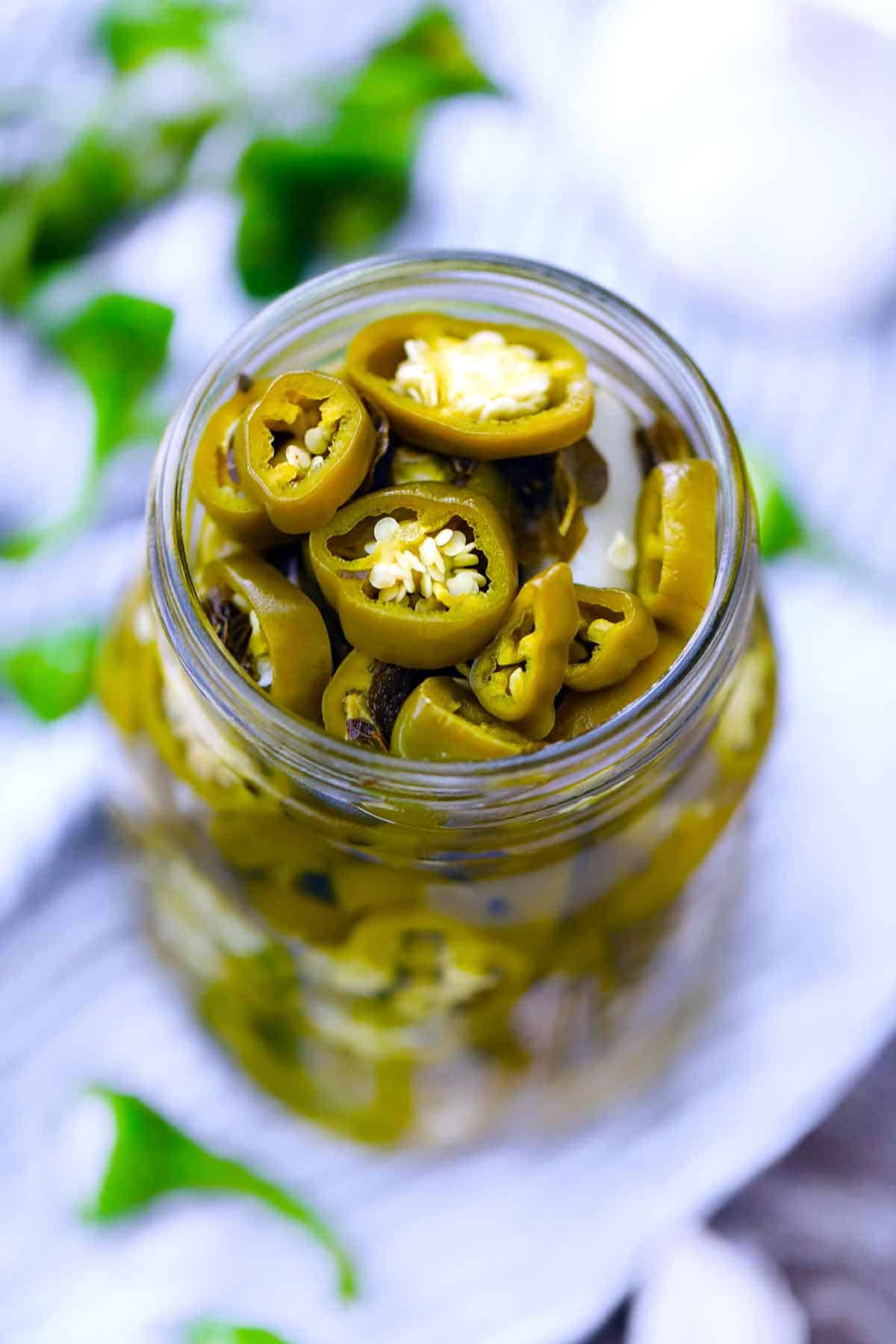 View from above of an open glass jar with pickled jalapeño peppers inside.