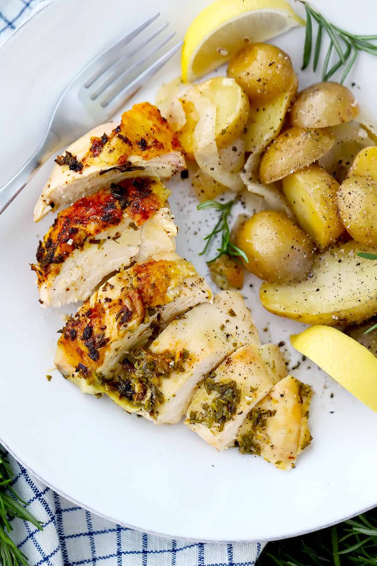 A sliced roasted chicken breast and potatoes on a white plate with a lemon slice.