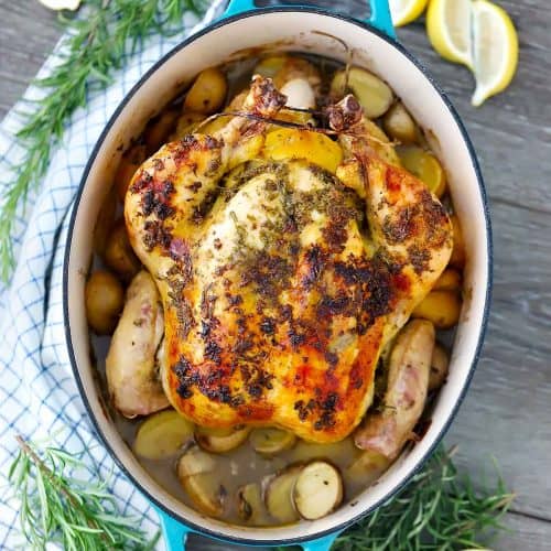 A whole chicken roasted in a blue cast iron enamel dutch oven with potatoes.