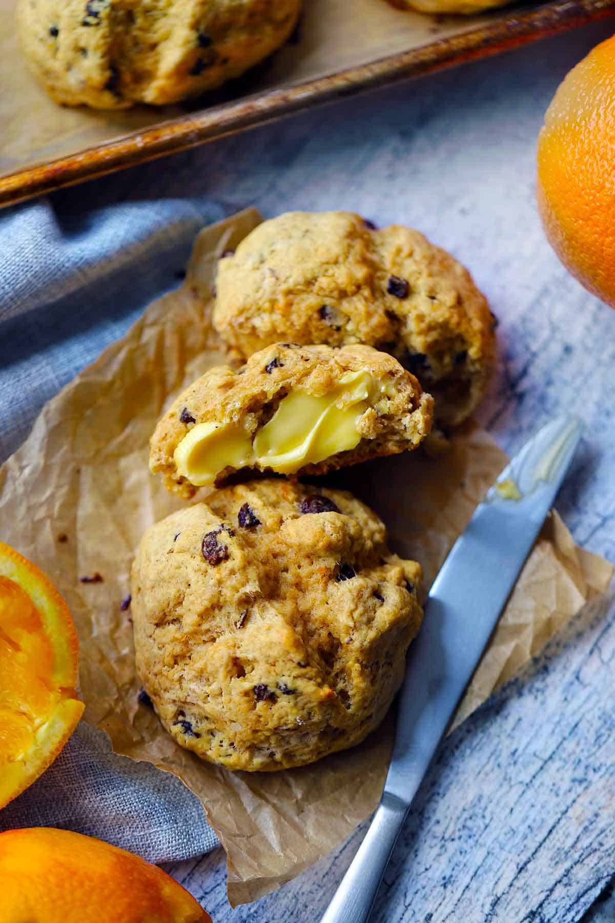 Irish soda bread scones, with oranges around, with one torn in half with butter on it.