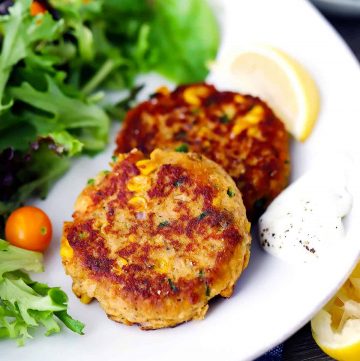 Two salmon cakes on a white plate with a lemon wedge and a salad.