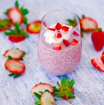 Square photo of a glass filled with strawberry chia seed pudding with chopped strawberries on top and whipped cream.