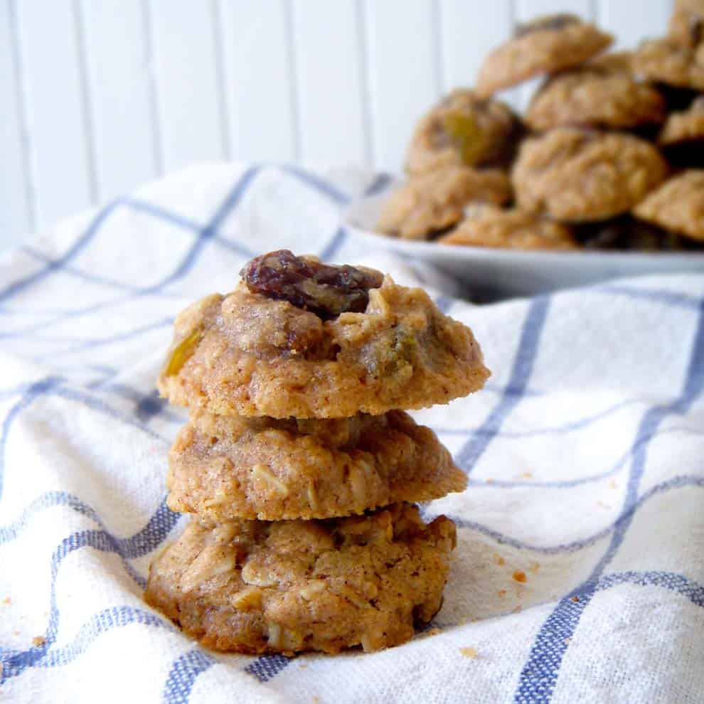 Three maple oatmeal raisin cookies stacked on a blue and white checkered cloth.