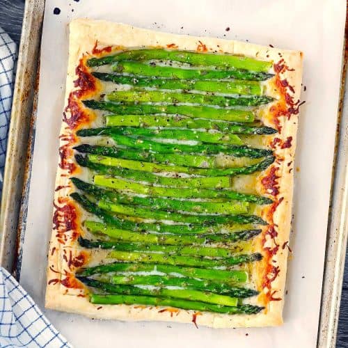 An asparagus tart made with puff pastry on a baking sheet on parchment paper.