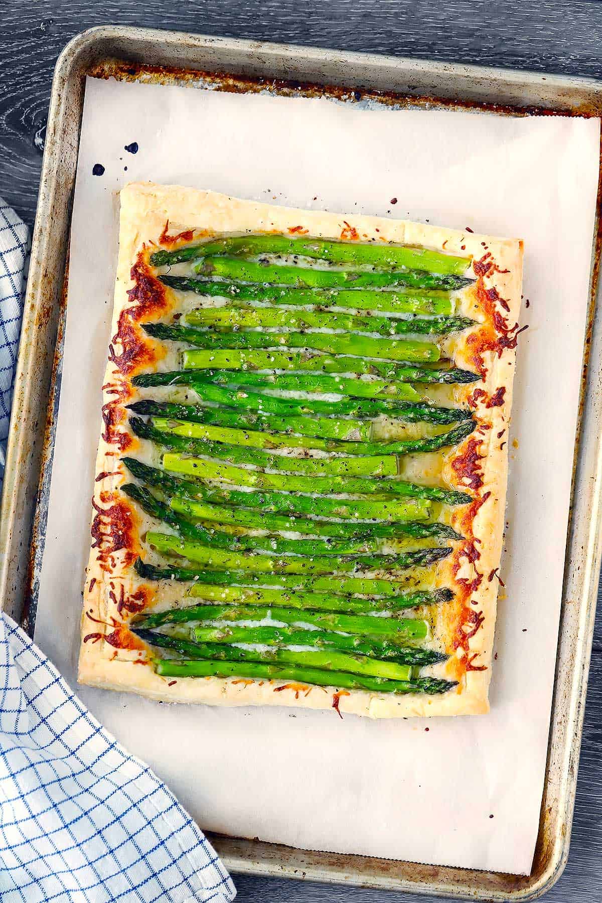 An asparagus tart made with puff pastry on a baking sheet on parchment paper.