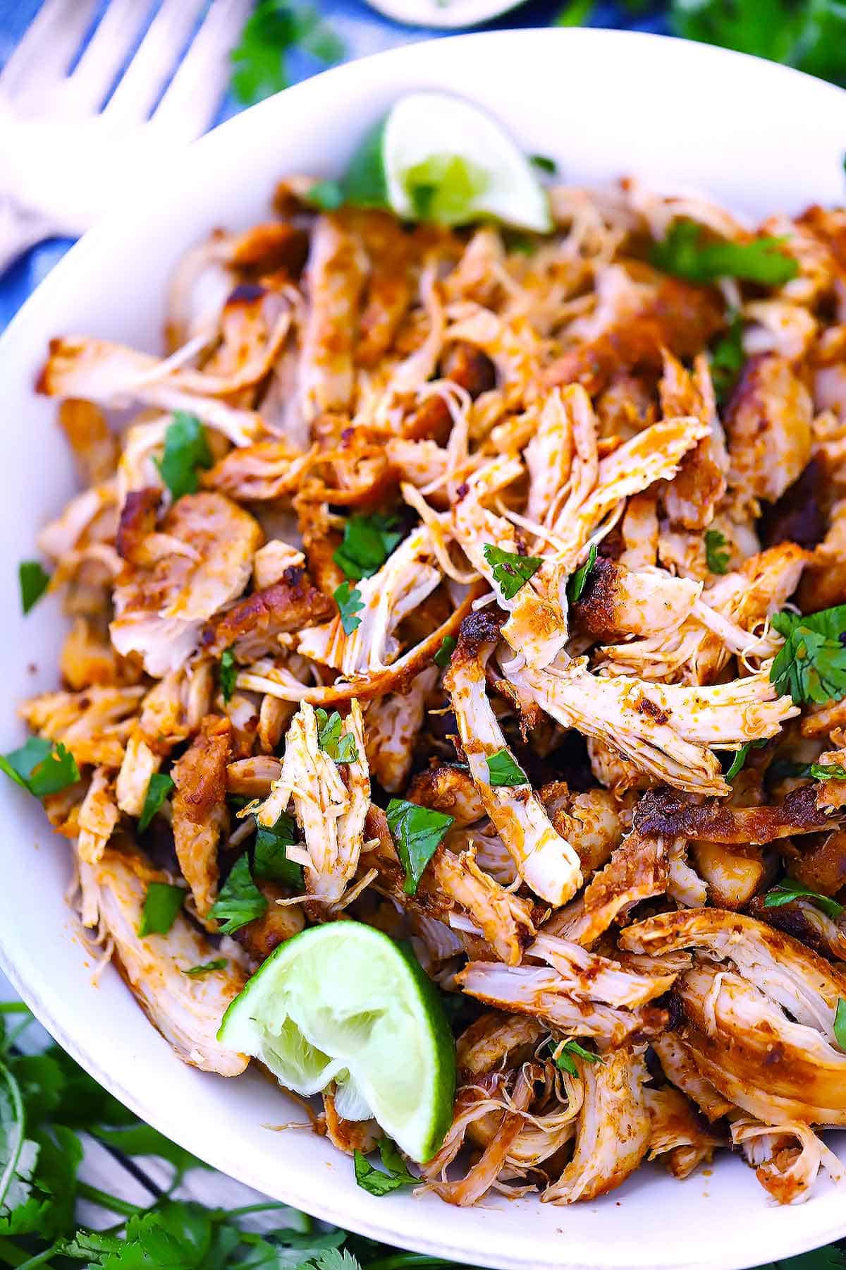 Close up overhead photo showing the texture of Mexican shredded chicken garnished with lime wedges and fresh cilantro.