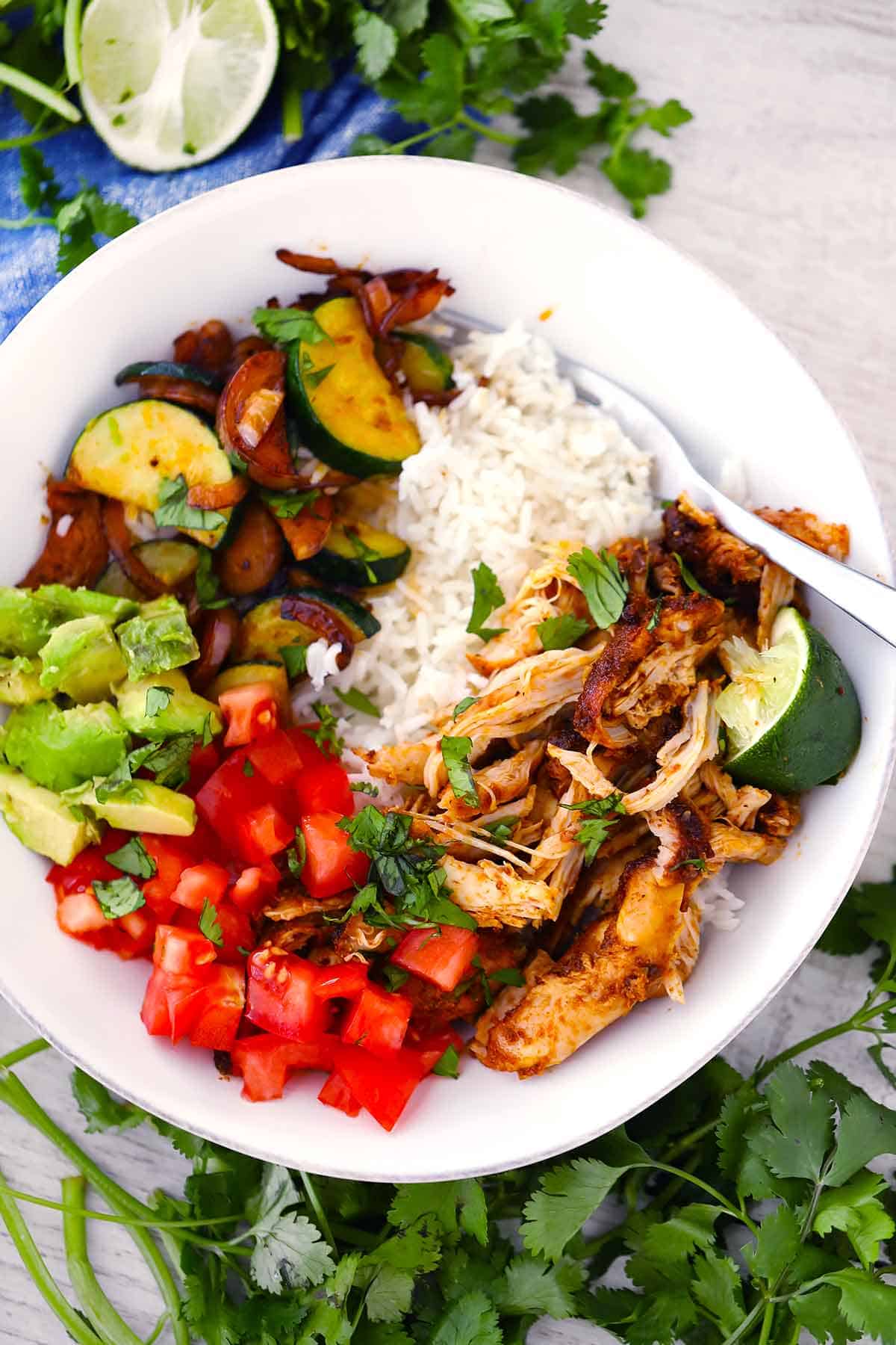 A burrito bowl with shredded chicken, veggies, avocado, tomato, and rice.