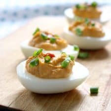 Deviled eggs on wooden cutting board. Closest one is in focus and remaining three are progressively out of focus as they move farther from camera.