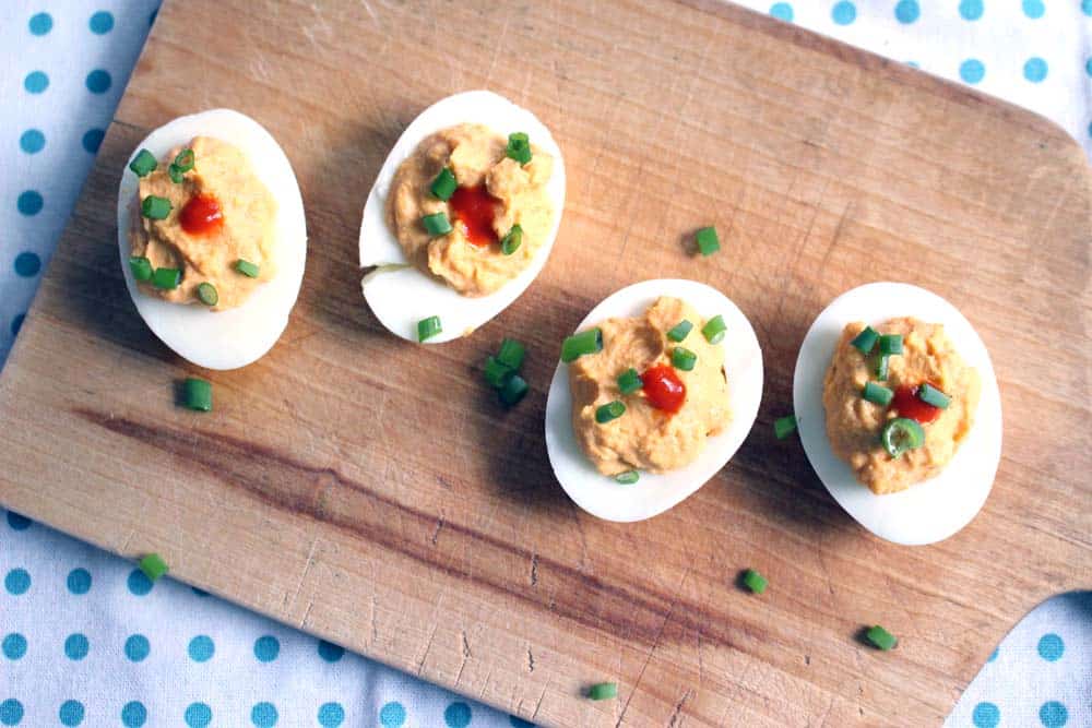 Bird's eye view of four deviled eggs on wooden cutting board.