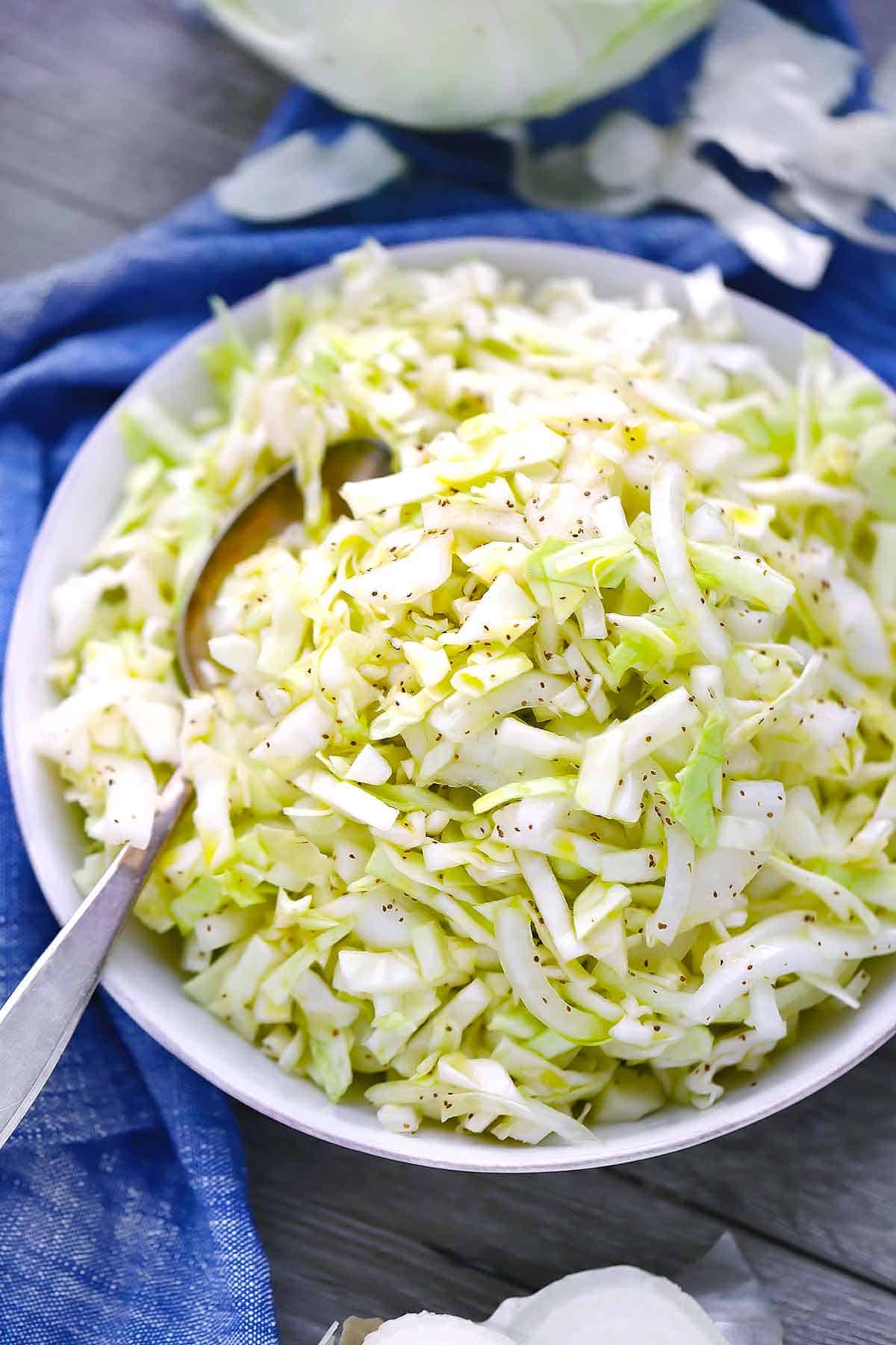A white bowl of no mayo coleslaw with celery seed and a spoon on a blue towel.
