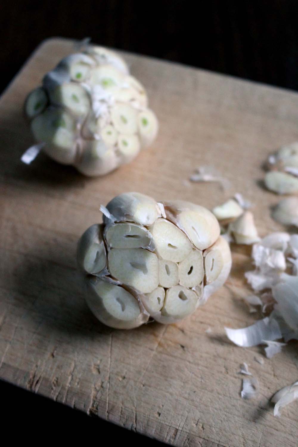 Heads of garlic cloves, one in foreground and one in background, with tops of garlic heads sliced off to reveal garlic inside.