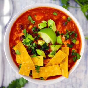 Square photo of smoked chicken tortilla soup topped with tortilla strips and avocado.
