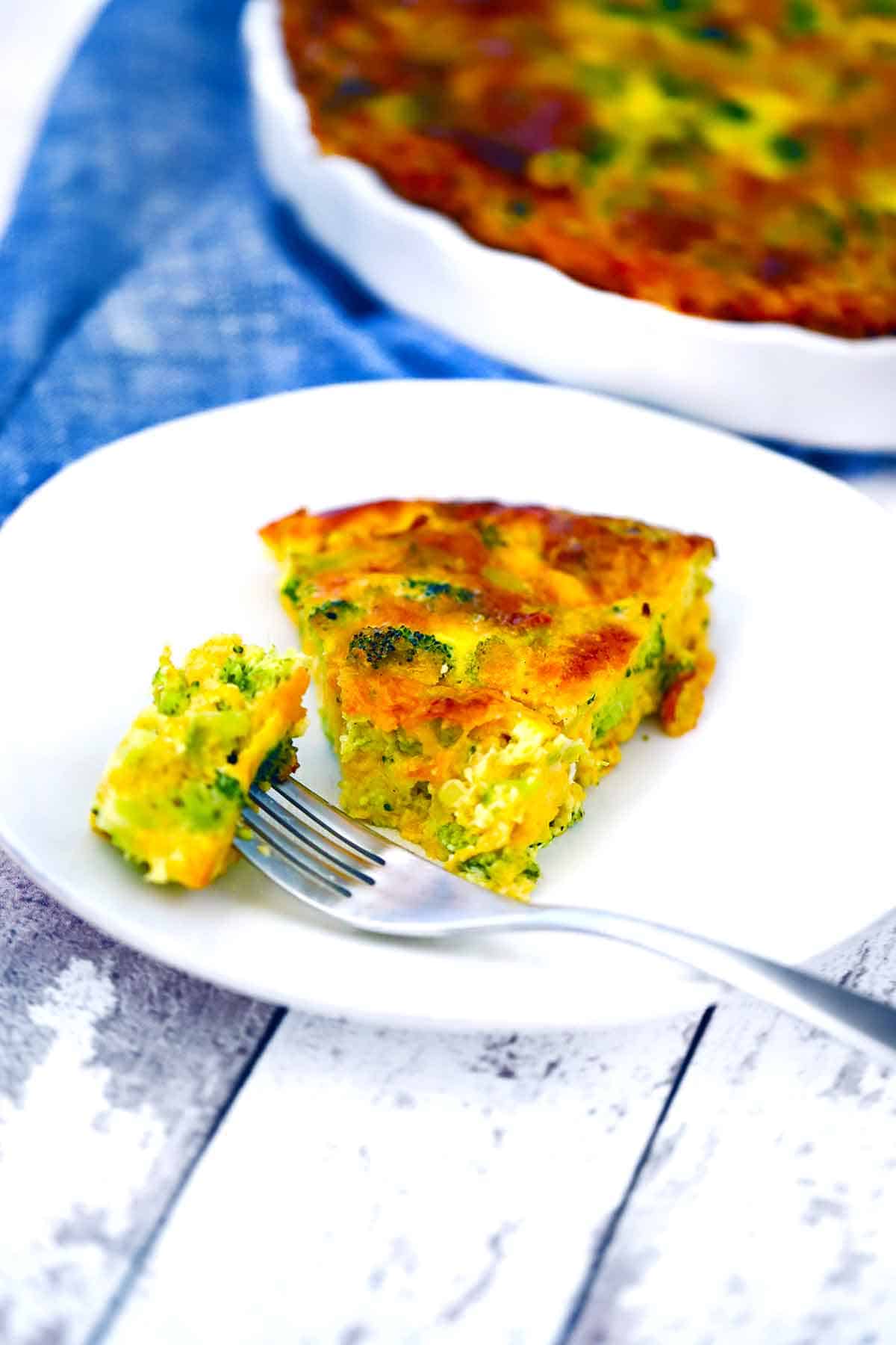A plate with a slice of broccoli quiche and a fork taking a bite out of it.