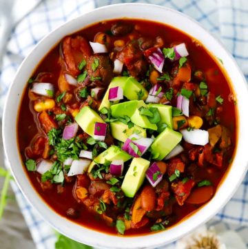 An overhead photo of a bowl of vegetarian chili with diced avocado, cilantro, and red onion on top.