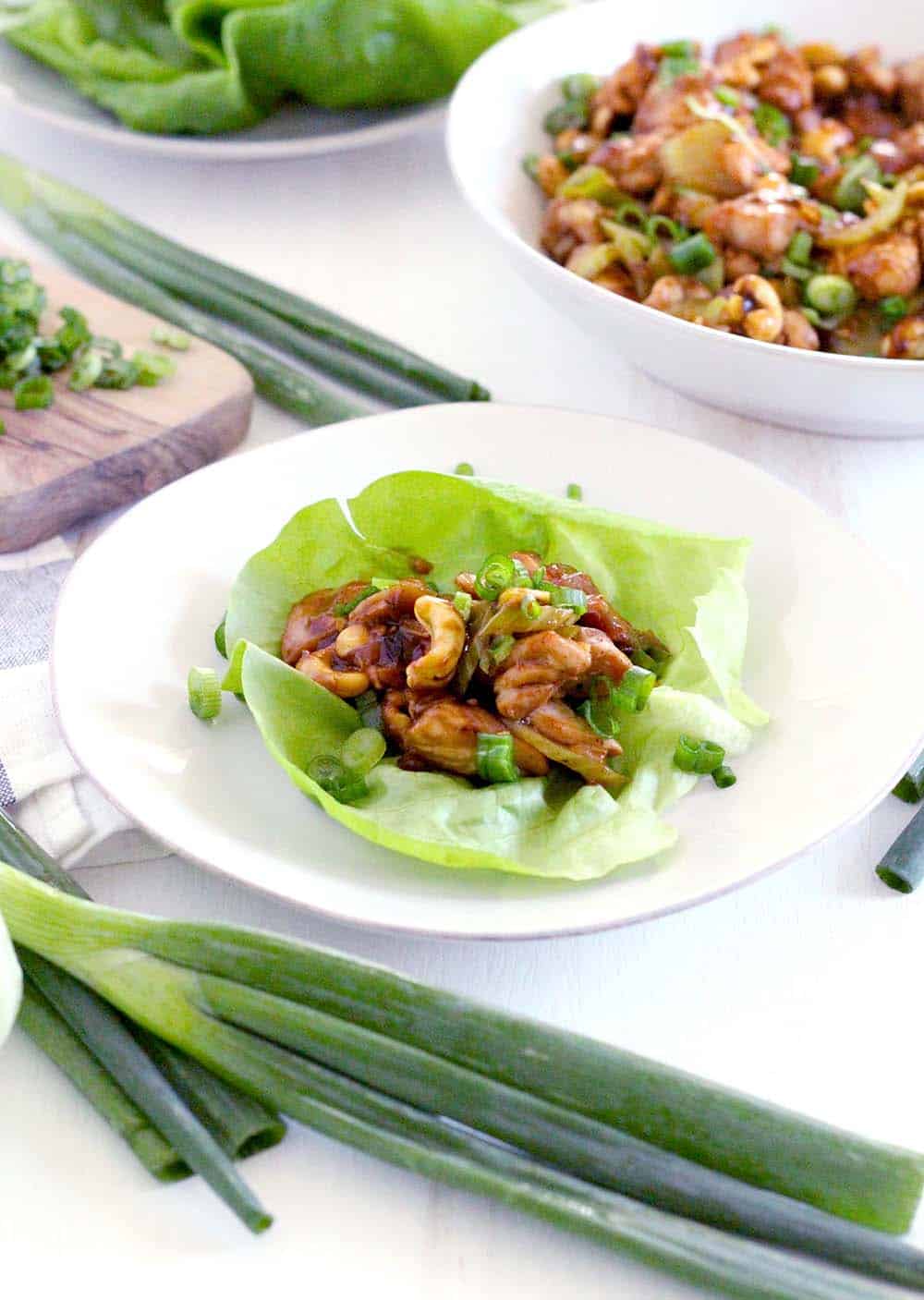 Open lettuce leaf on a white plate, with chicken and cashew mixture placed in the center.