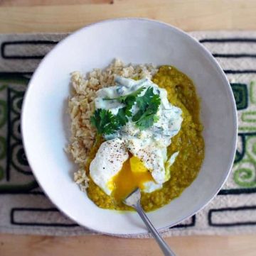 Red Lentil Dal viewed from above, in a white plate with poached egg and fork piercing the egg yolk.