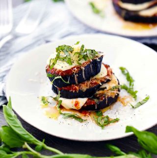 Roasted eggplant parmesan stack on a white plate with fresh basil chiffonade on top