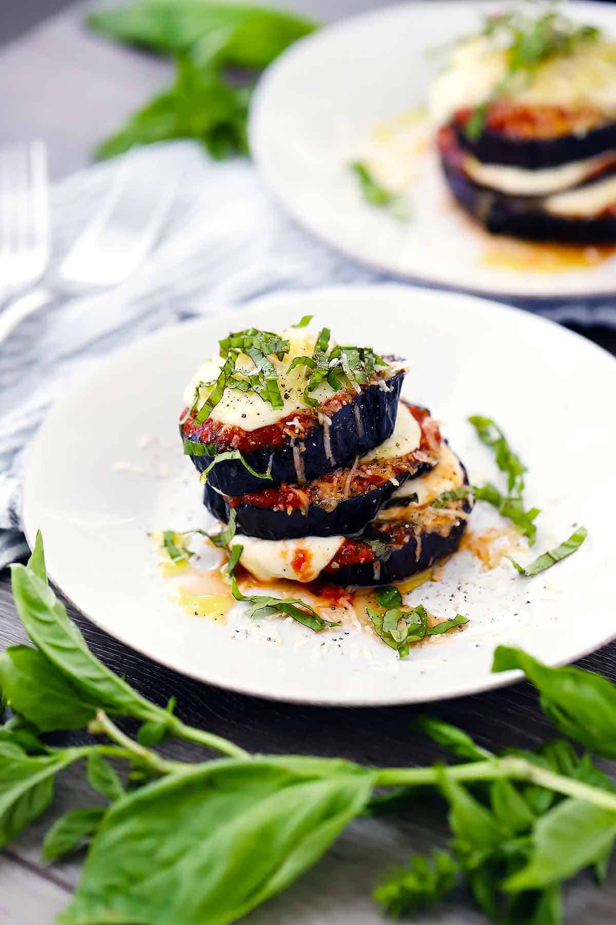 Roasted eggplant parmesan stack on a white plate with fresh basil chiffonade on top