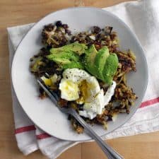 Bird's eye view of a white plate holding veggie burger hash browns, sliced avocado, a poached egg, and a fork.