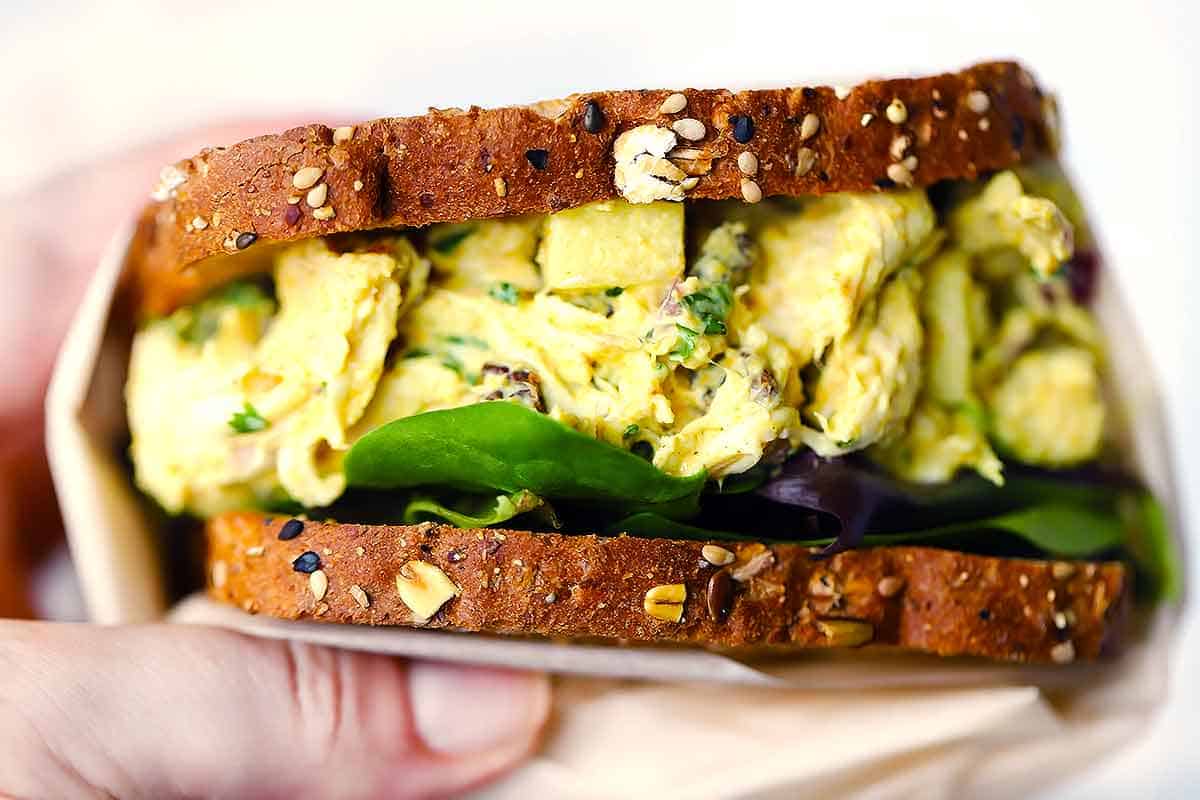 Close up photo of a hand holding a curried chicken salad sandwich.