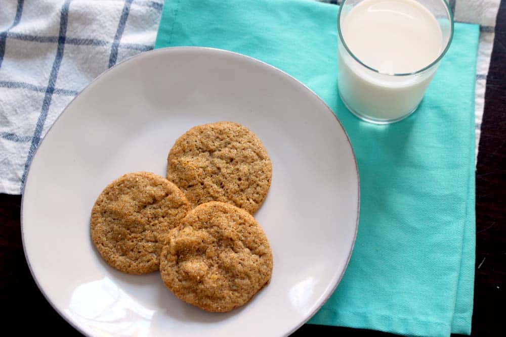 Bird's eye view of three cookies on a white plate, on a turquoise cloth with a glass of milk on the side.