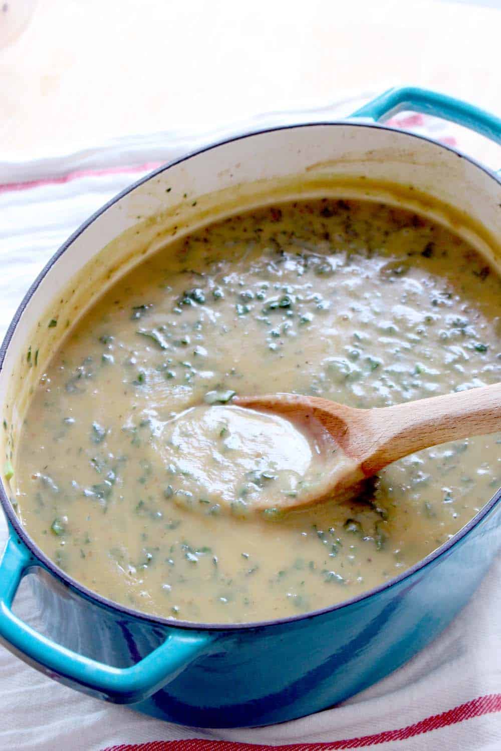 Dutch oven filled with creamy soup, with a wooden spoon perched inside.