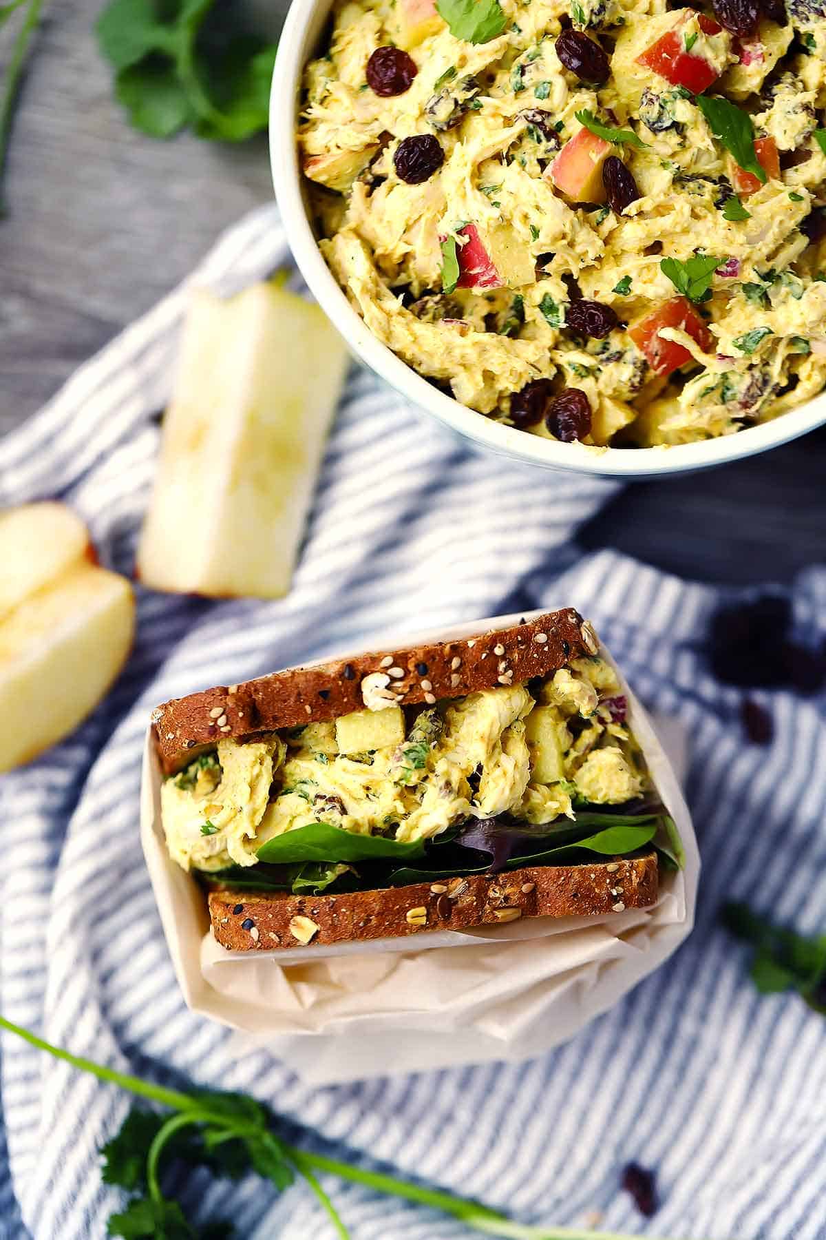 A curried chicken salad sandwich next to a bowl on a towel wrapped in parchment paper.